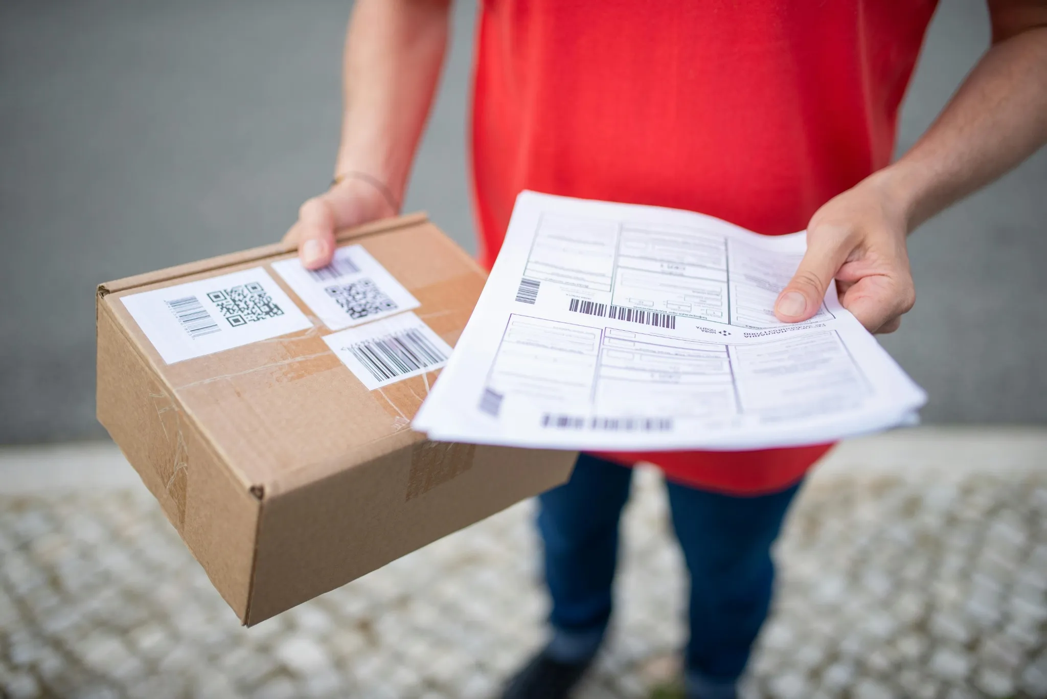 Mão a segurar encomenda e guias de transporte com códigos de barras.